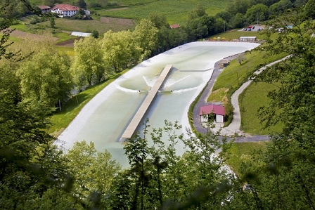 Ein künstlicher See mit einem Steg in der Mitte. Rechts und links Wellen und Surfer